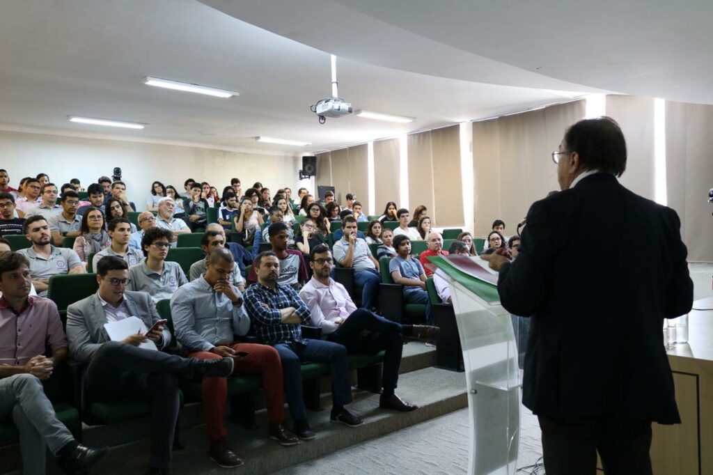 Descrição da imagem: foto mostra Renato Sabbatini de costas, no canto esquerdo da tela, durante sua palestra. Um auditório lotado está na frente dele, as pessoas prestam atenção. 
