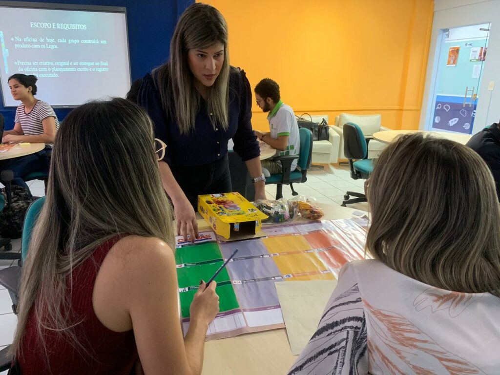 Descrição da imagem: A ministrante da oficina, Milena Duarte dá explicações para uma dupla de participantes.